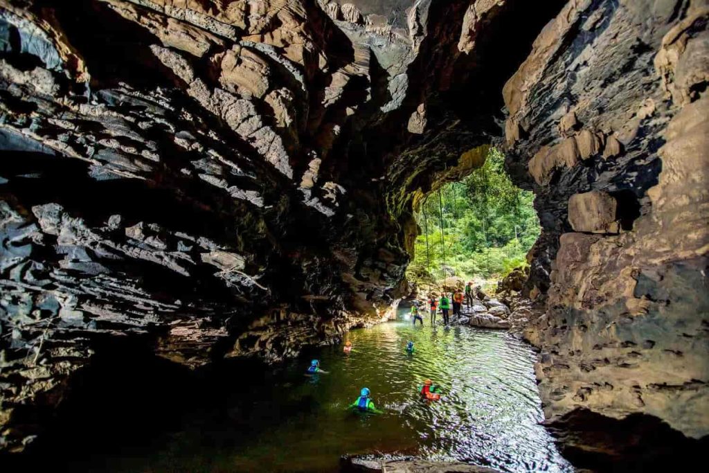 Underground waterfalls in the Tu Lan Cave System, surrounded by ancient trees and limestone mountains.