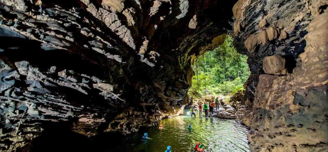 Underground waterfalls in the Tu Lan Cave System, surrounded by ancient trees and limestone mountains.