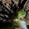 Underground waterfalls in the Tu Lan Cave System, surrounded by ancient trees and limestone mountains.